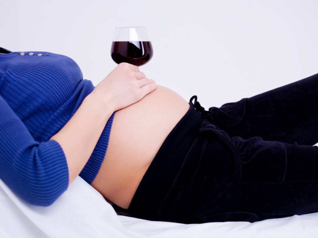 Glass of wine on top of pregnant woman's stomach